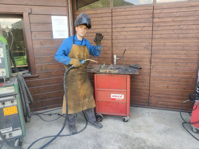 M. Salamin portant un casque et un tablier se tient devant une machine à souder. | JB Salamin Métal-création