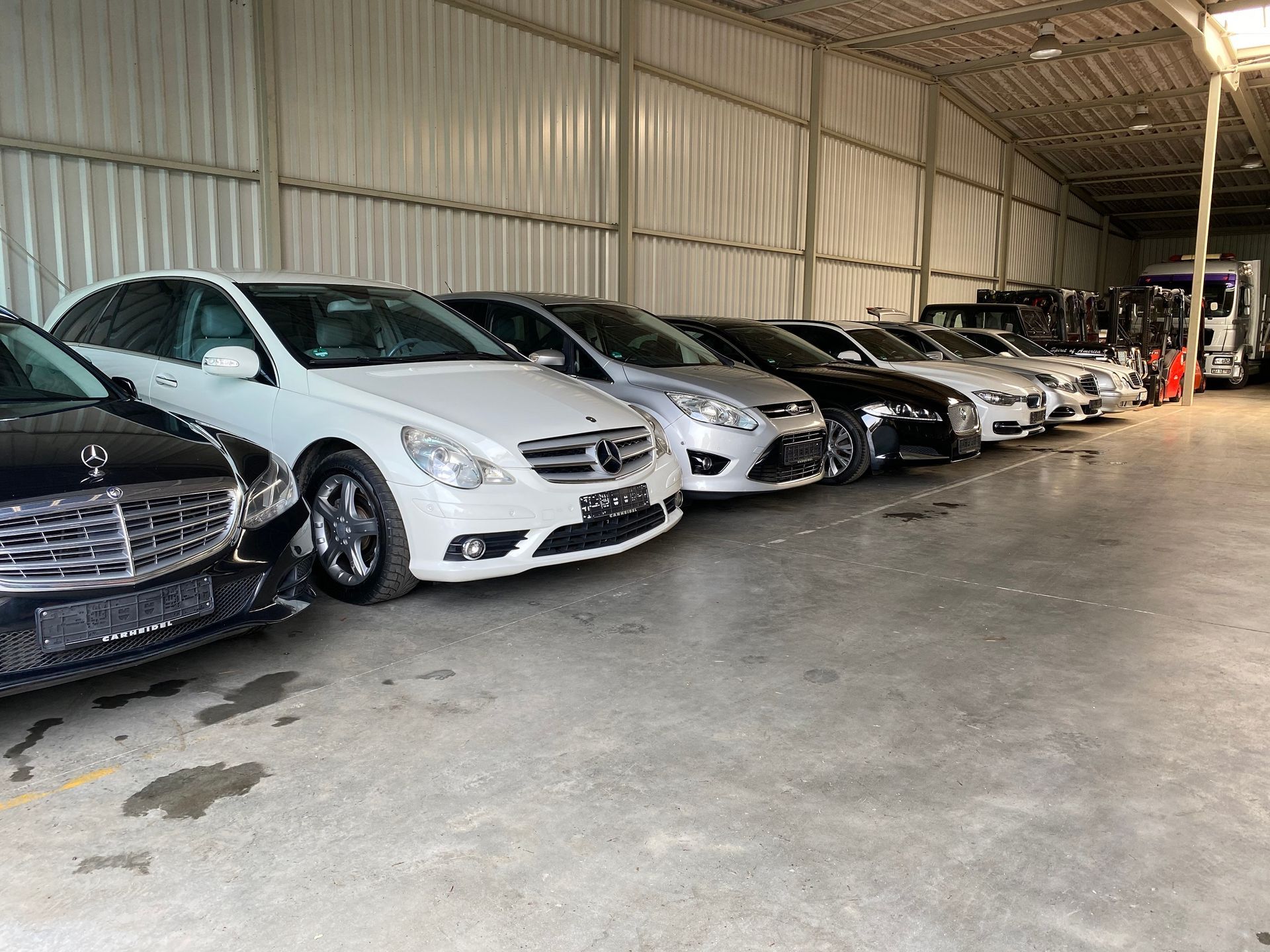 Eine Reihe von Autos parkt in einem Lagerhaus mit grauem Betonboden und Wellblechwänden.