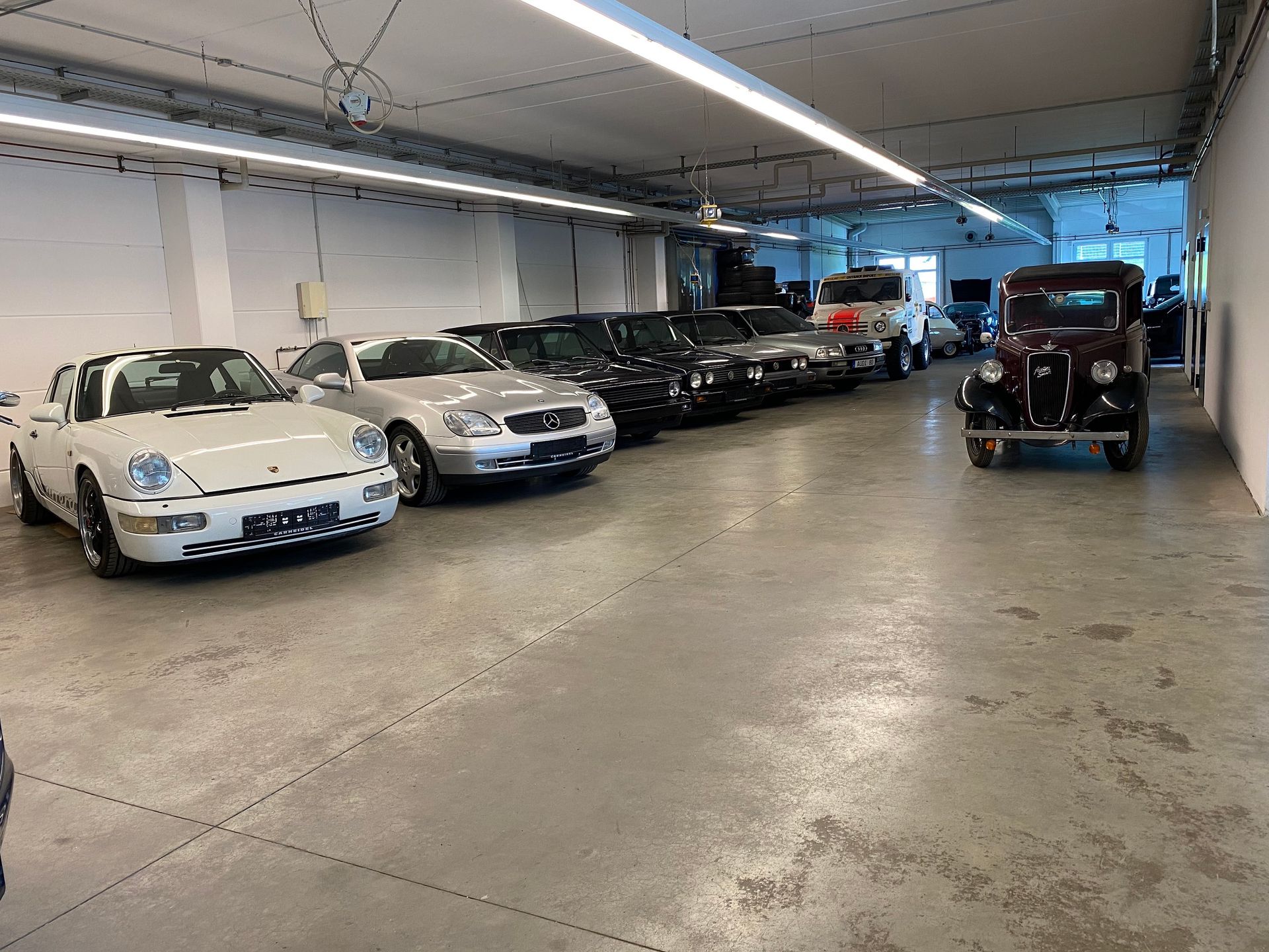 In einer Garage geparkte Autos, darunter ein weißer Porsche und ein altes schwarzes Fahrzeug.