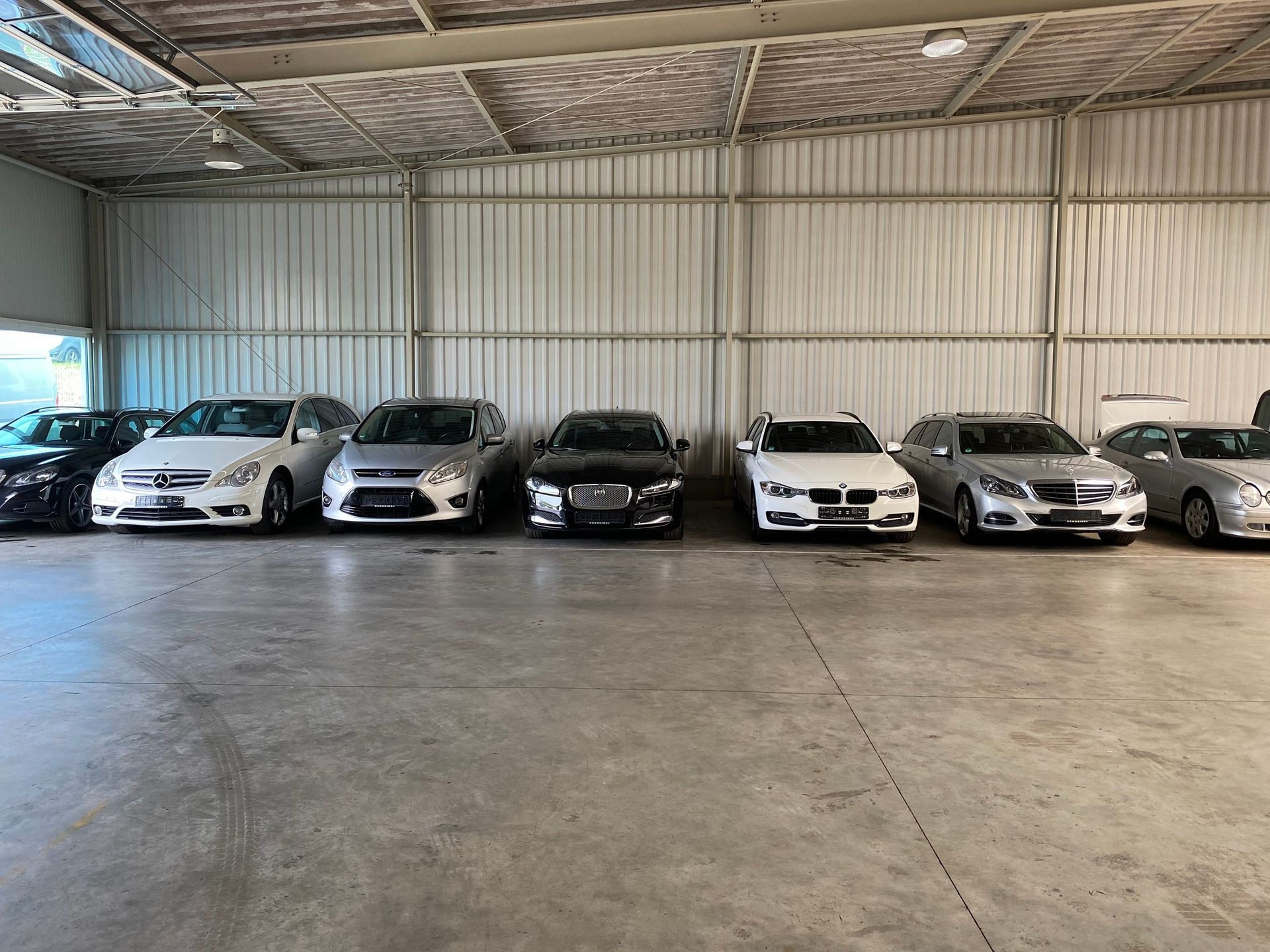 In einem Lagerhaus geparkte Autos. Verschiedene Farben, darunter Schwarz, Weiß und Silber.