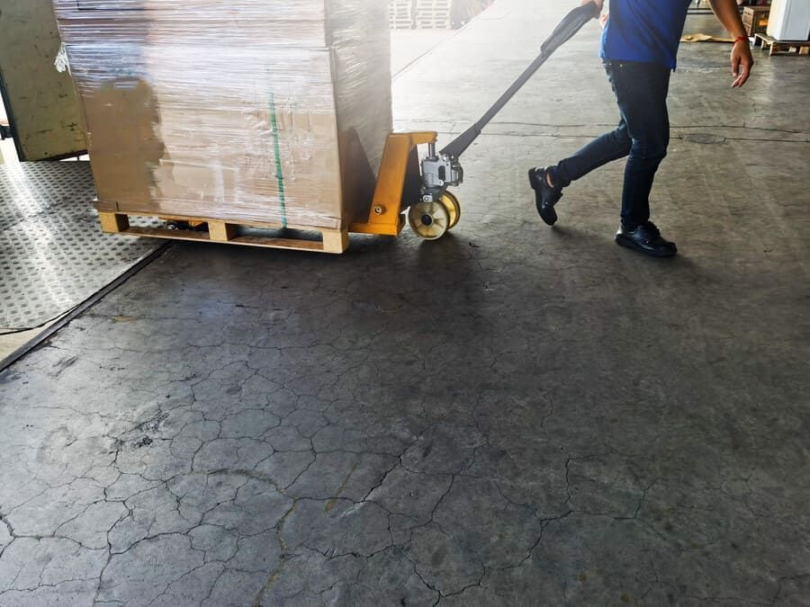 Un hombre empuja una paleta con cajas sobre ella en un almacén.