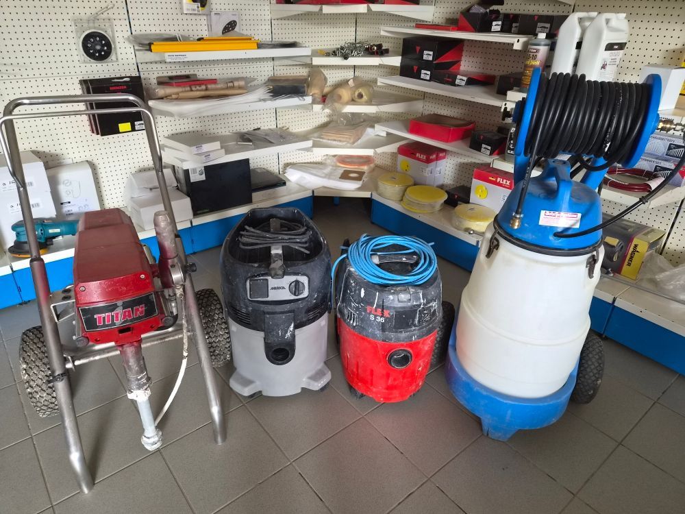 Étagère d'atelier avec des aspirateurs eau et poussière rouges, gris et bleus et un enrouleur de tuyau bleu sur la droite