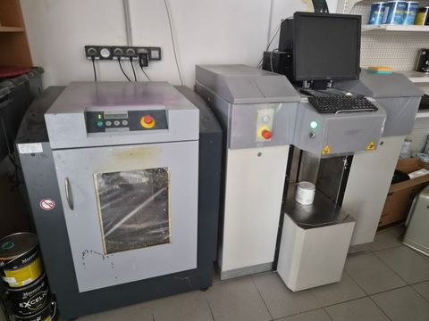 Deux machines industrielles grises avec panneaux de commande dans un atelier, l'une d'elles avec une vitre avant transparente.