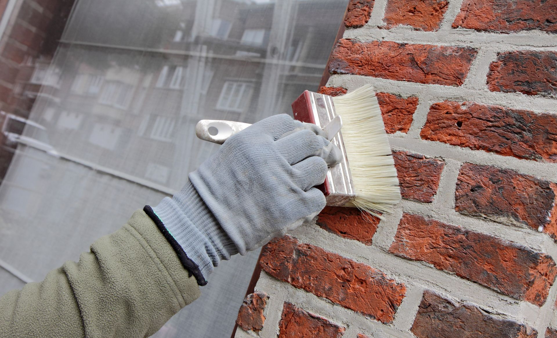 Une main gantée applique un produit hydrophobe à l'aide d'un pinceau brosse sur un mur en brique