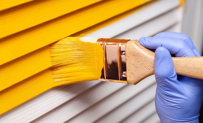 Une main gantée applique de la peinture jaune sur un mur en bois