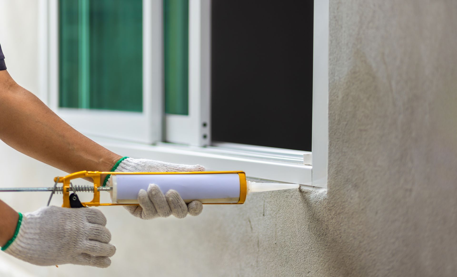Un artisan applique du silicone sur la bordure d'une fenêtre à l'aide d'un pistolet applicateur