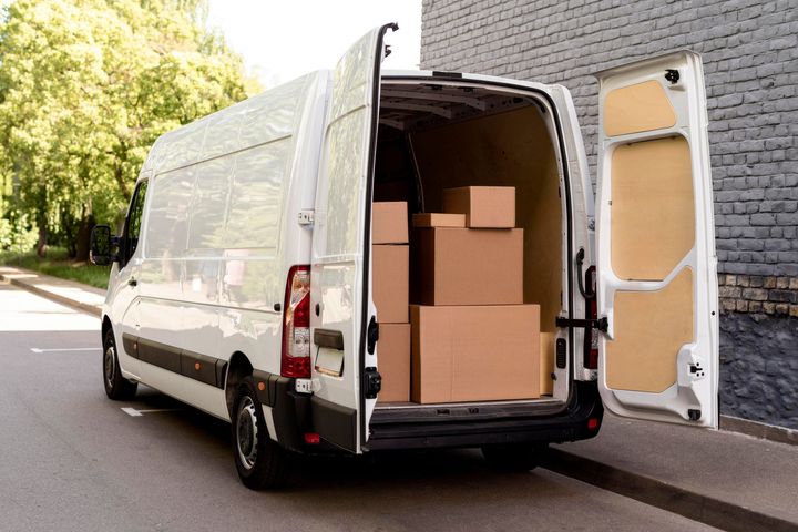 Una camioneta de reparto blanca llena de cajas está estacionada al costado de la carretera.