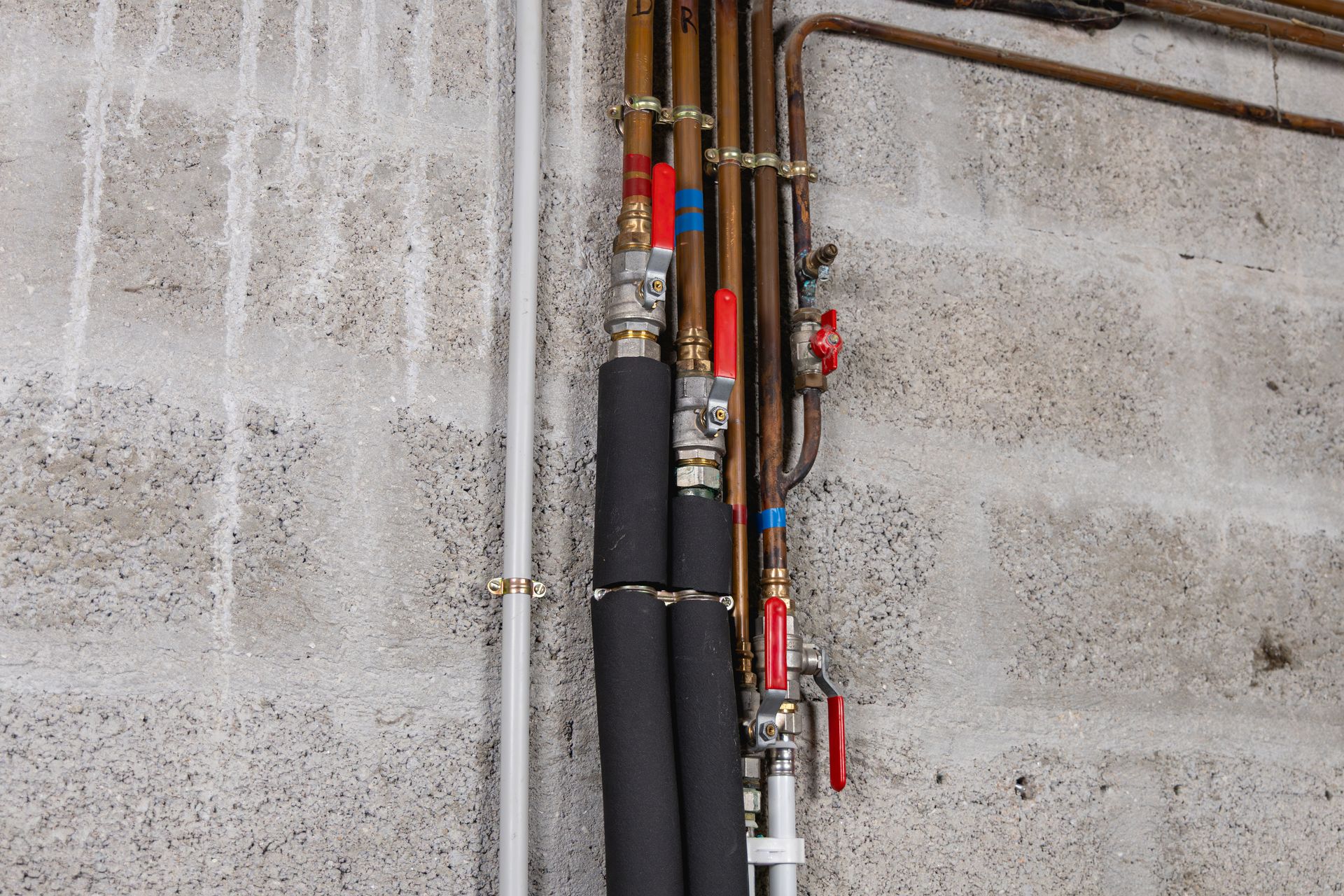 Des tuyaux en cuivre avec des vannes rouges et bleues fixées à un mur en parpaings.