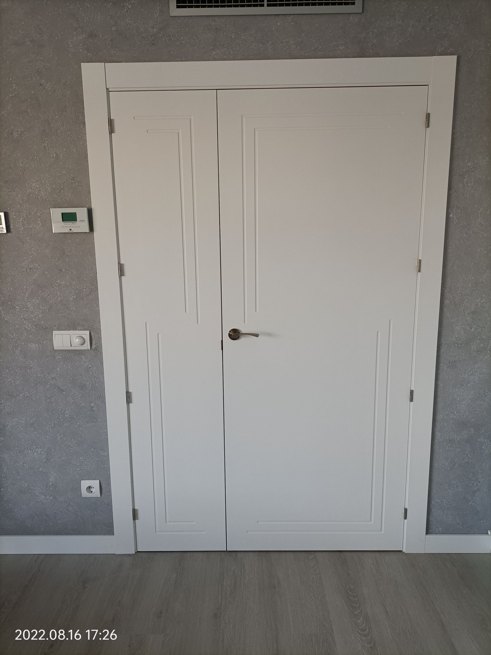 Una puerta blanca en una habitación con un termostato en la pared.