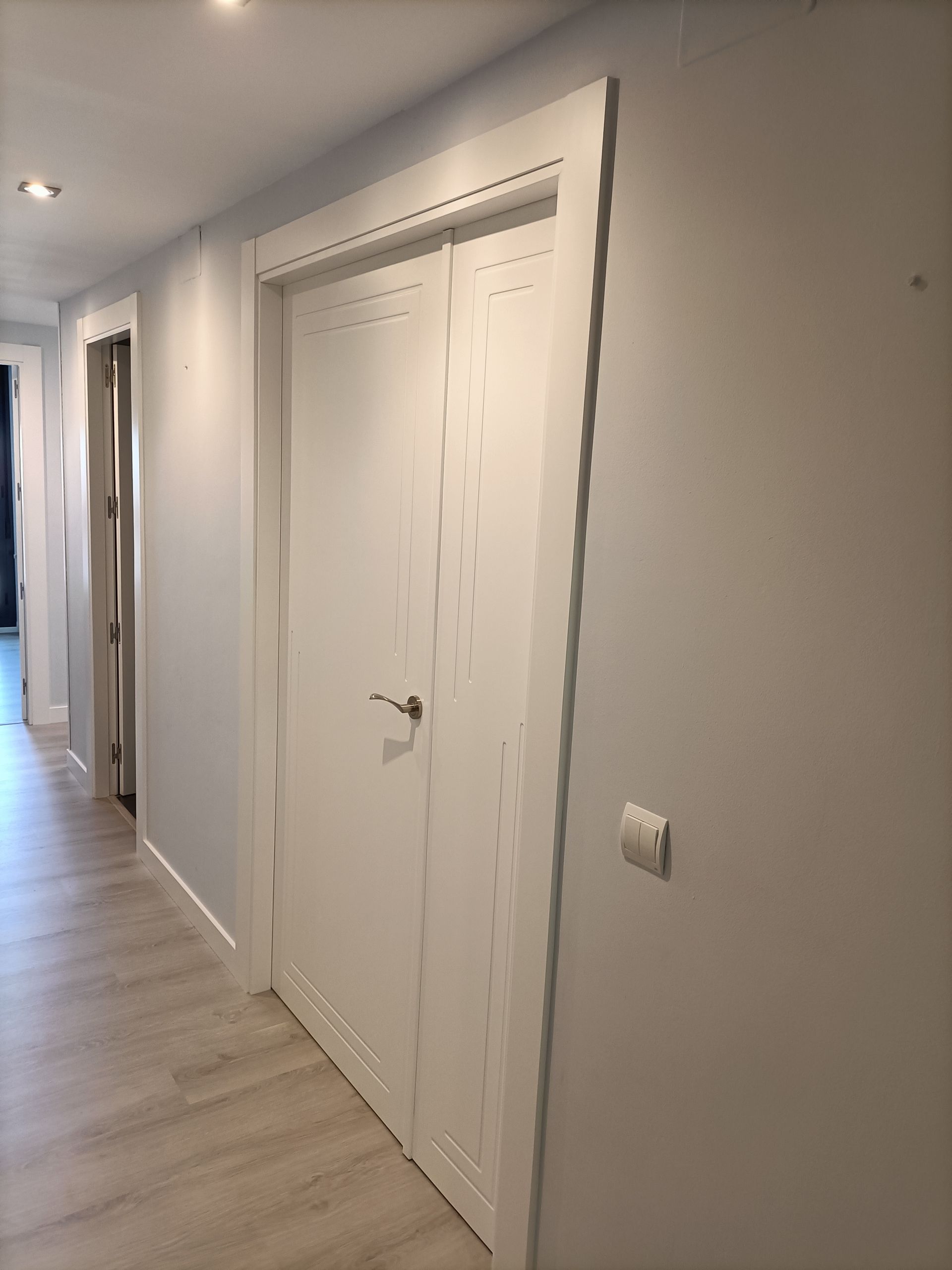 Un largo pasillo con puertas blancas y suelo de madera.