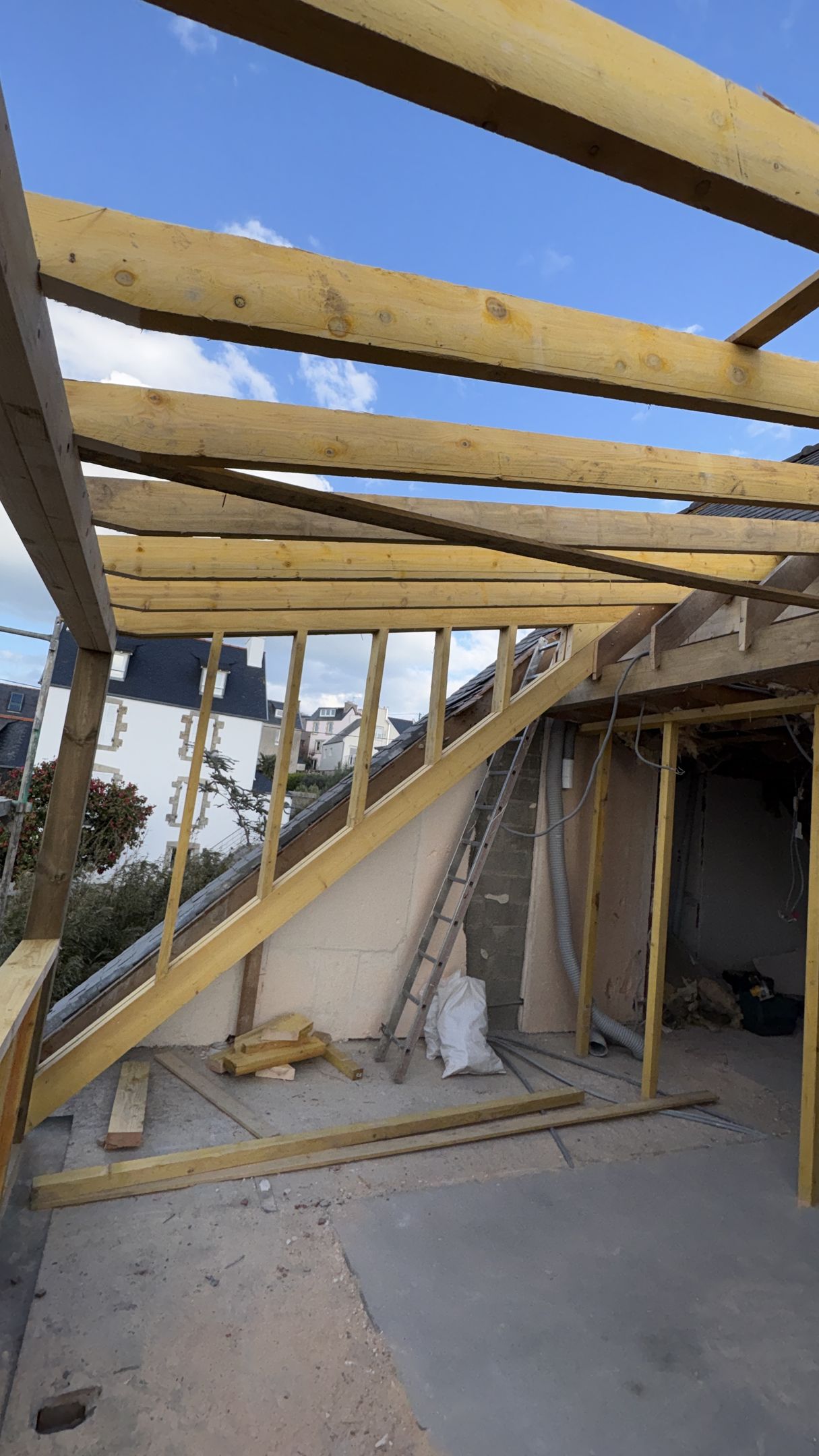 Toiture partiellement charpentée en construction avec poutres en bois apparentes et dalle en béton en dessous