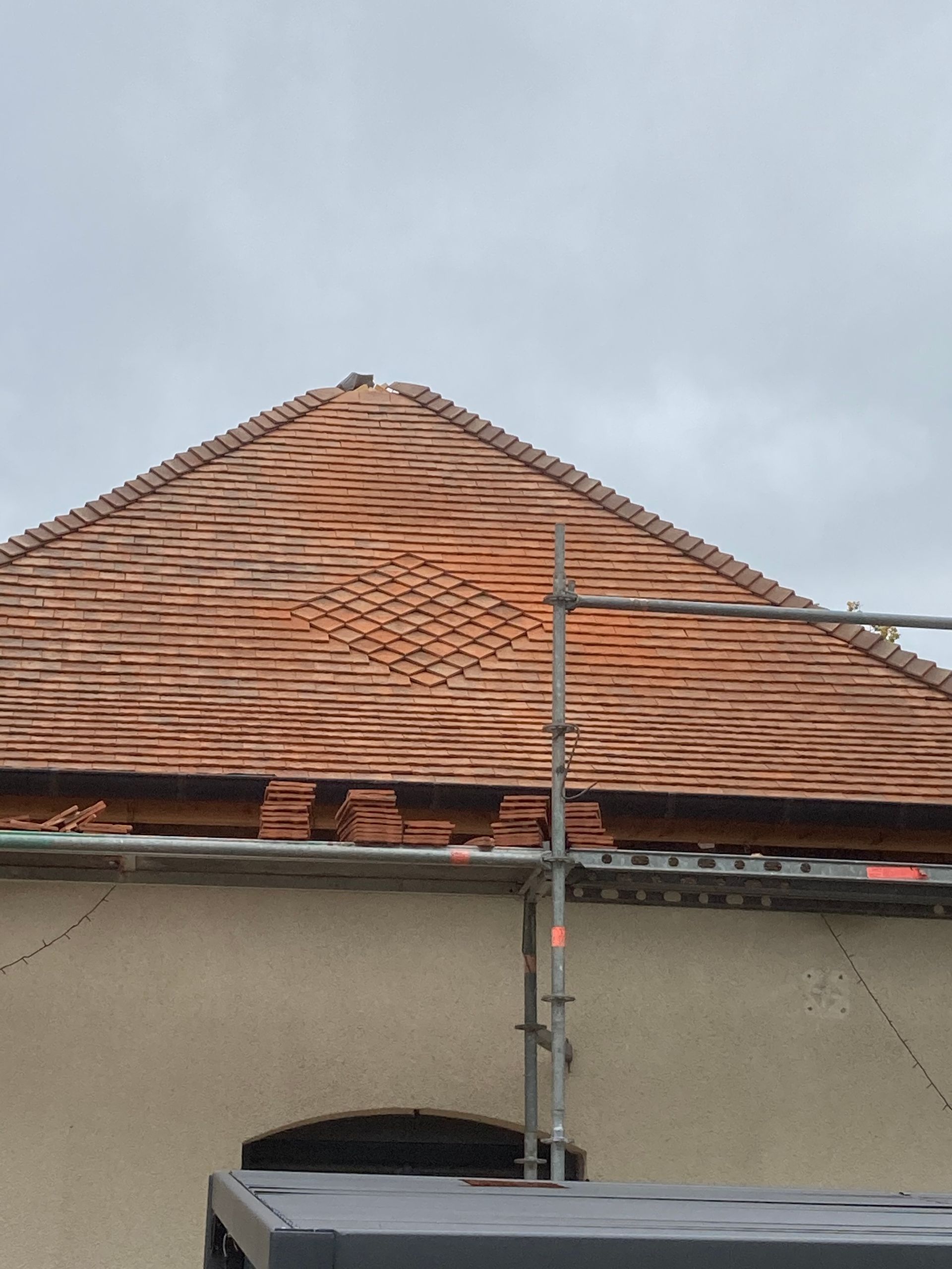 Toit de tuiles rouges sous un ciel nuageux, avec un poteau vertical et un mur d'immeuble en dessous.