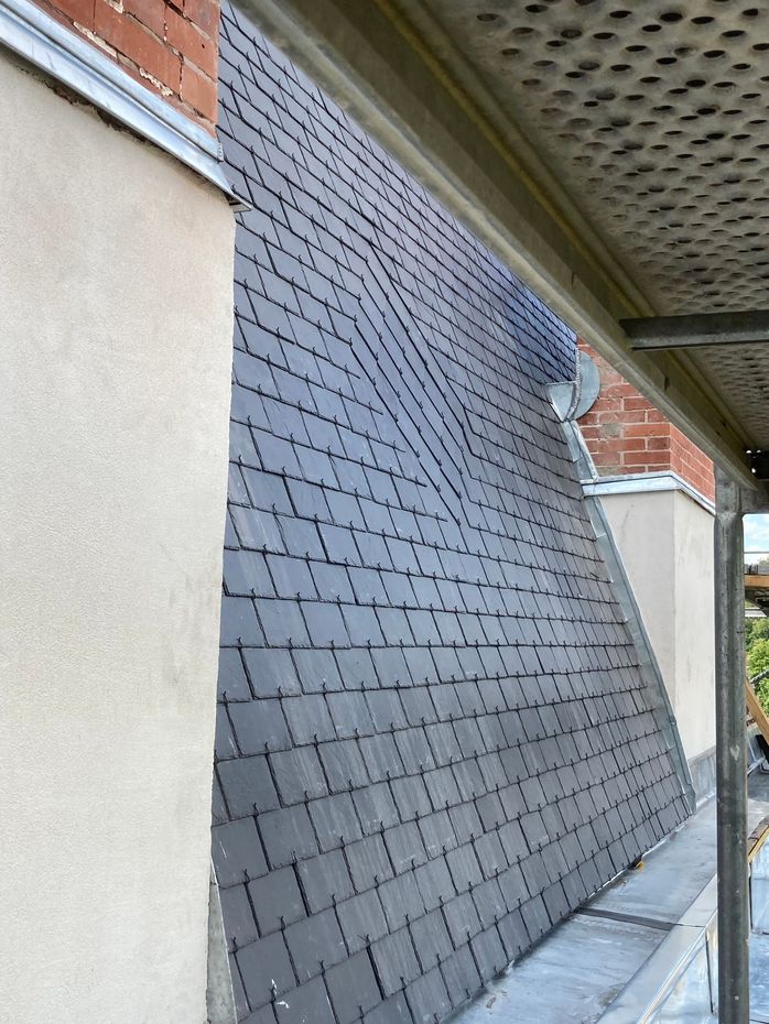 Grande section de toit en ardoise appuyée contre un mur à côté d'un bâtiment sous un avant-toit.
