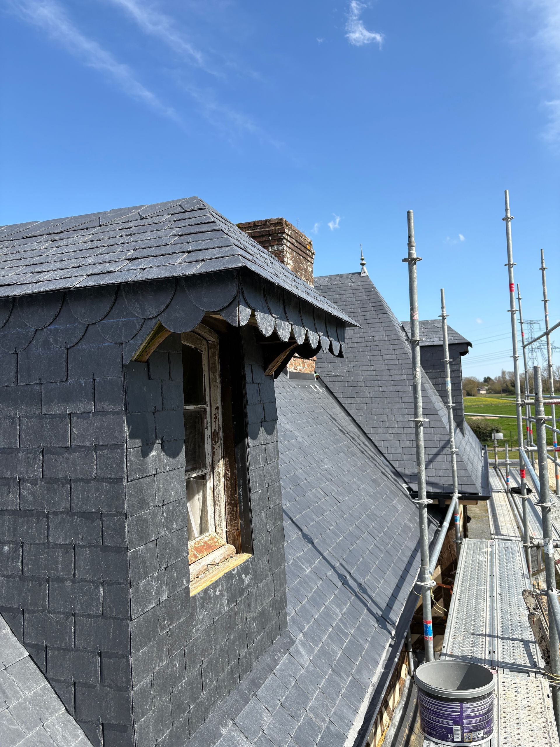 Travaux de toiture sur une maison gris foncé avec échafaudages sous un ciel bleu clair
