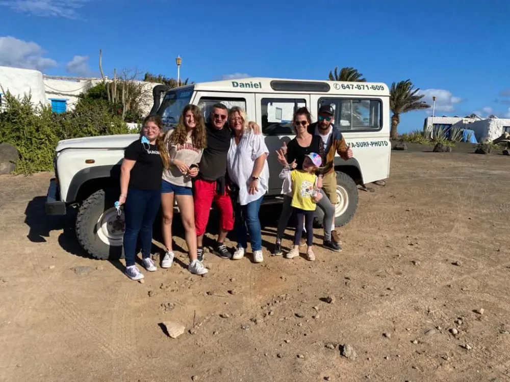 Un grupo de ocho personas posan para una foto frente a un vehículo todoterreno blanco estacionado en un terreno de tierra bajo un cielo soleado.