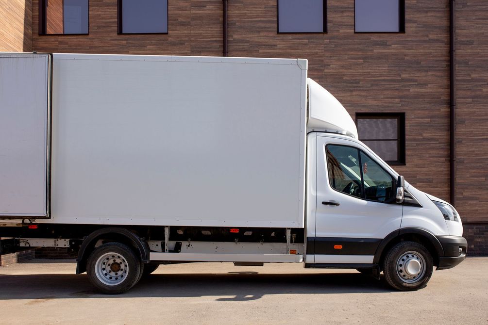 Un camion fourgon blanc garé à côté d’un bâtiment en briques.