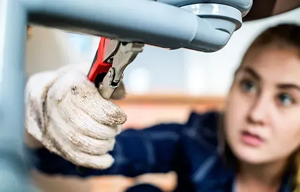 Una mujer está arreglando una tubería con una llave inglesa.