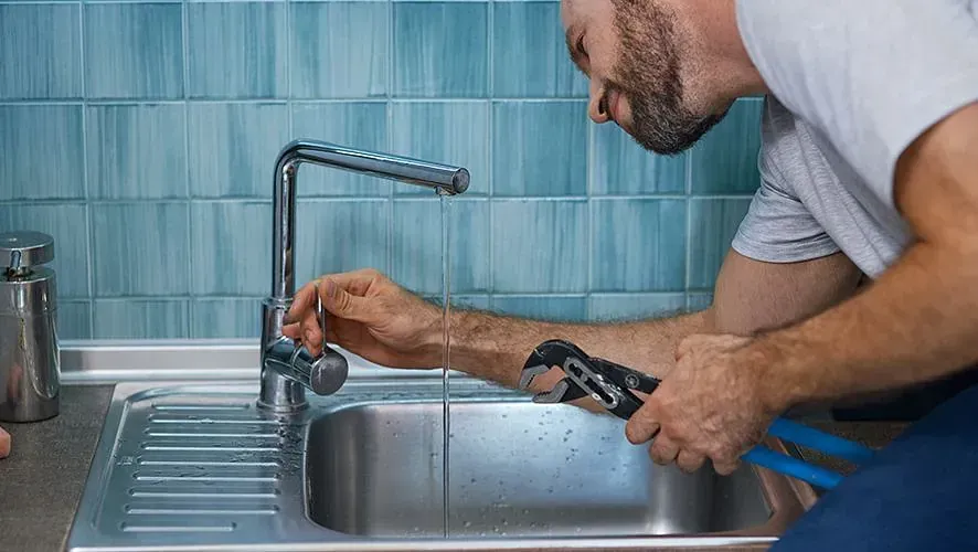 Un hombre está arreglando un grifo en un fregadero de cocina con una llave inglesa.