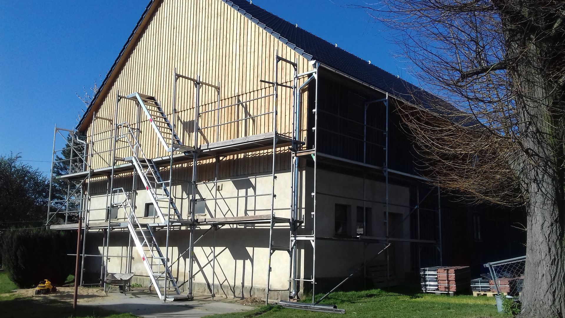 Hausfassade während der Sanierung mit Holzverkleidung und Baugerüst an der Außenwand.