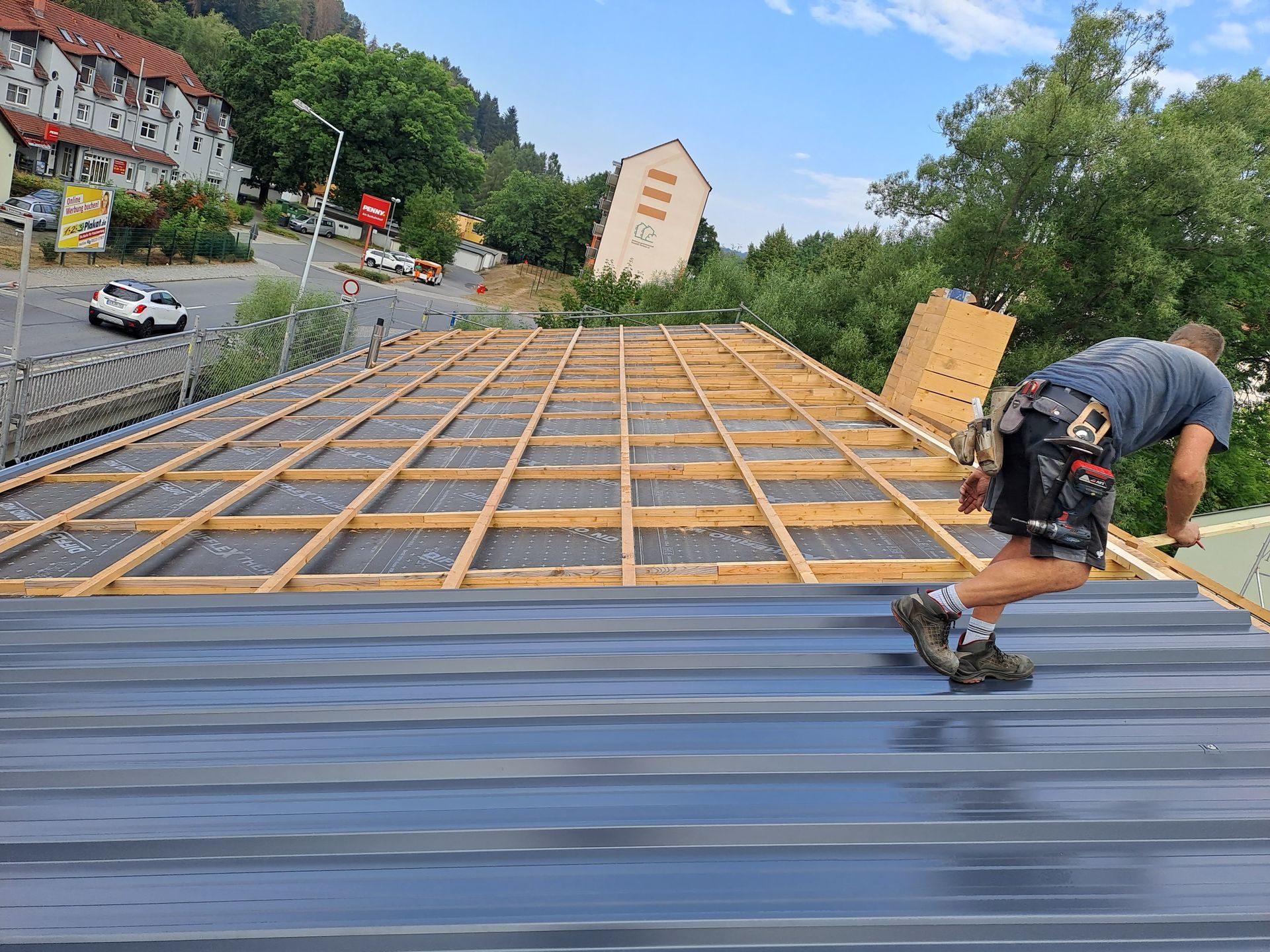 Dachmontage mit Holzlattung und Verlegung von Trapezblechen durch einen Arbeiter auf der Baustelle.