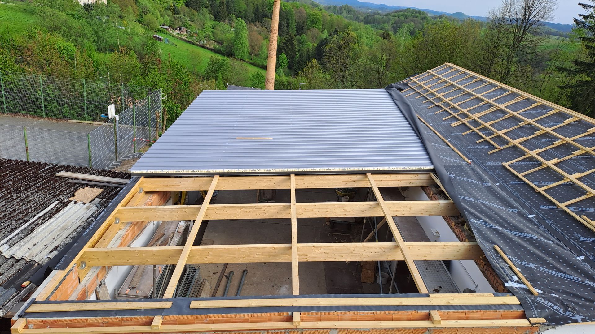 Teilweise fertiggestelltes Dach mit verlegten Trapezblechen auf einer Holzlattung in Hanglage.
