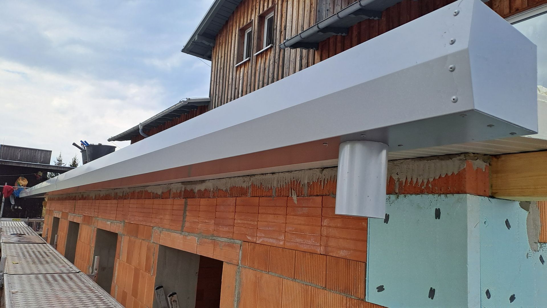 Montierte Sandwichpaneele als Dachabschluss mit Dachrinne an einem Ziegelrohbau.