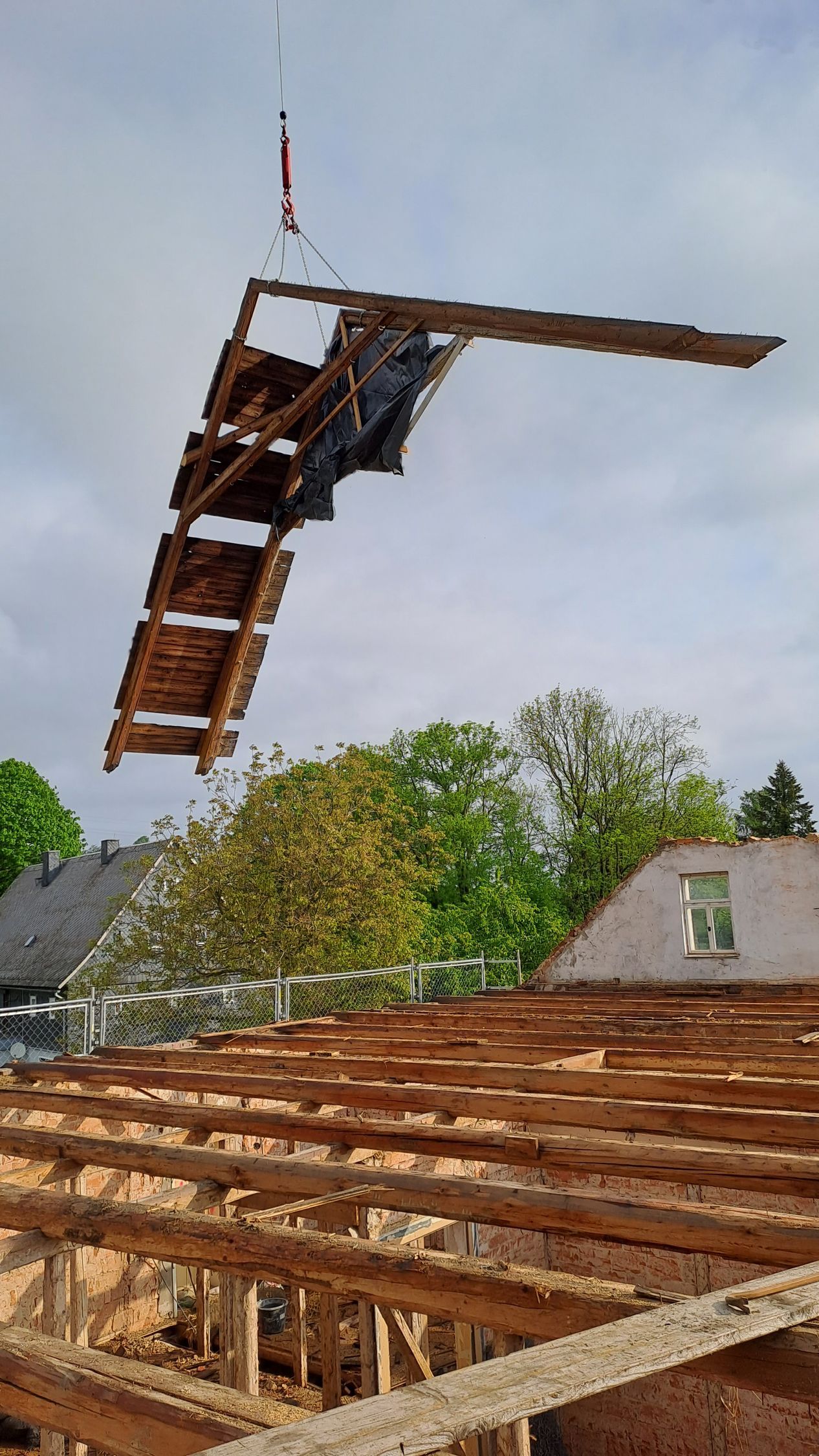 Kran hebt vorgefertigtes Holzelement über ein Gebäude auf einer Baustelle.