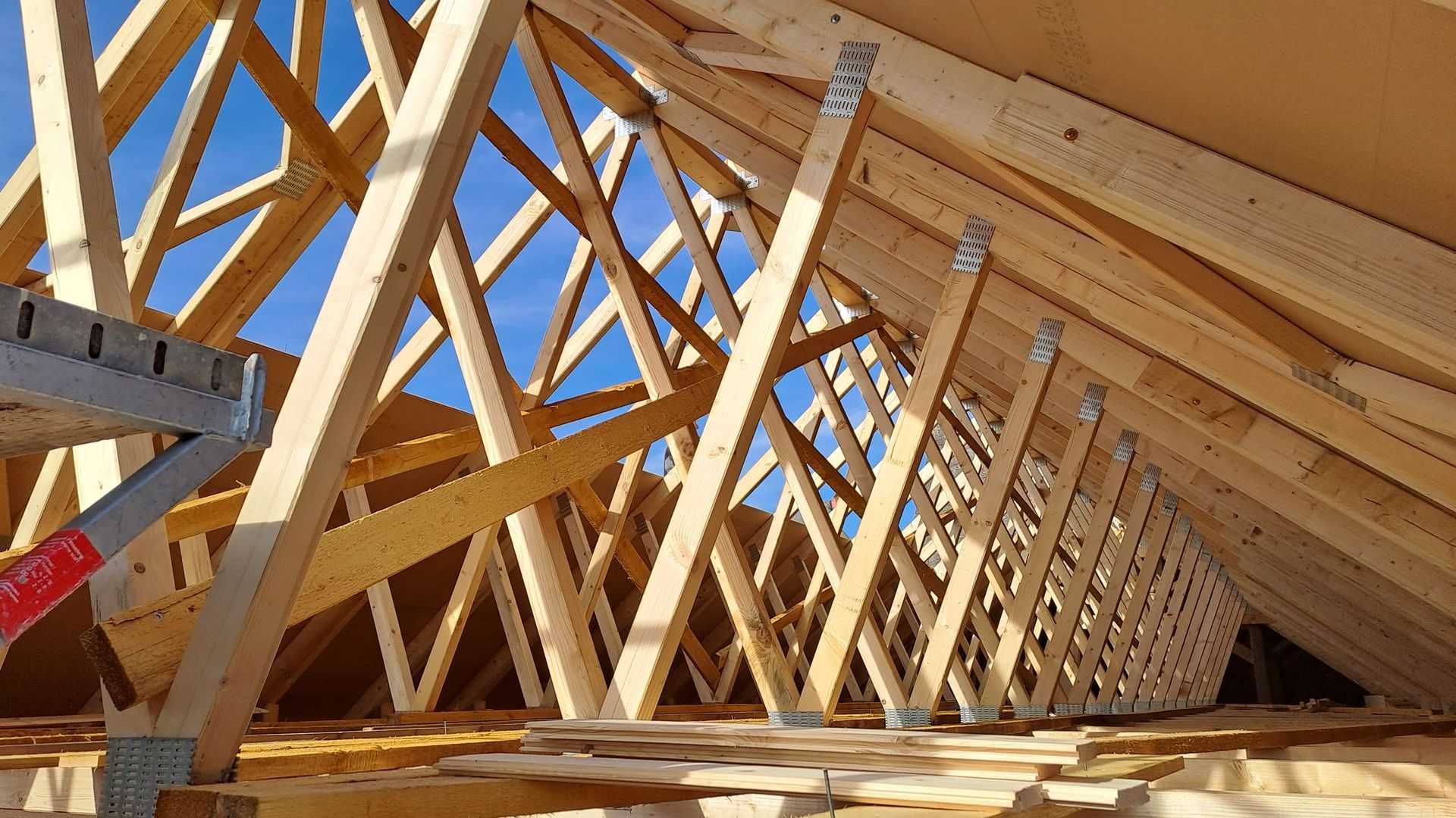 Innenansicht eines Dachstuhls mit symmetrischen Holzsparren und Querstreben unter blauem Himmel.