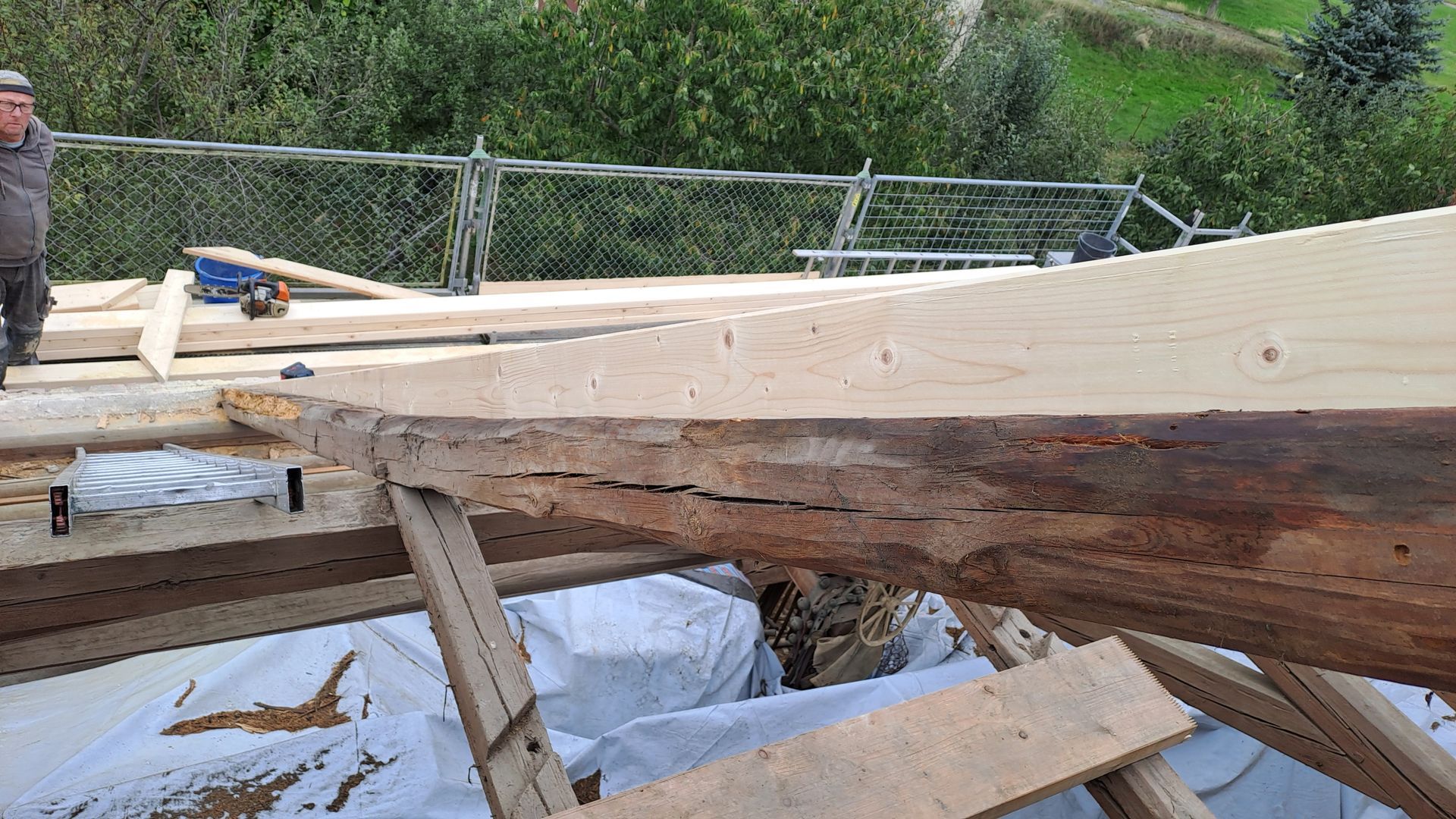 Rohes Holztragwerk auf Baustelle mit Baumstamm-Balken und gesägten Holzbrettern im Vordergrund.