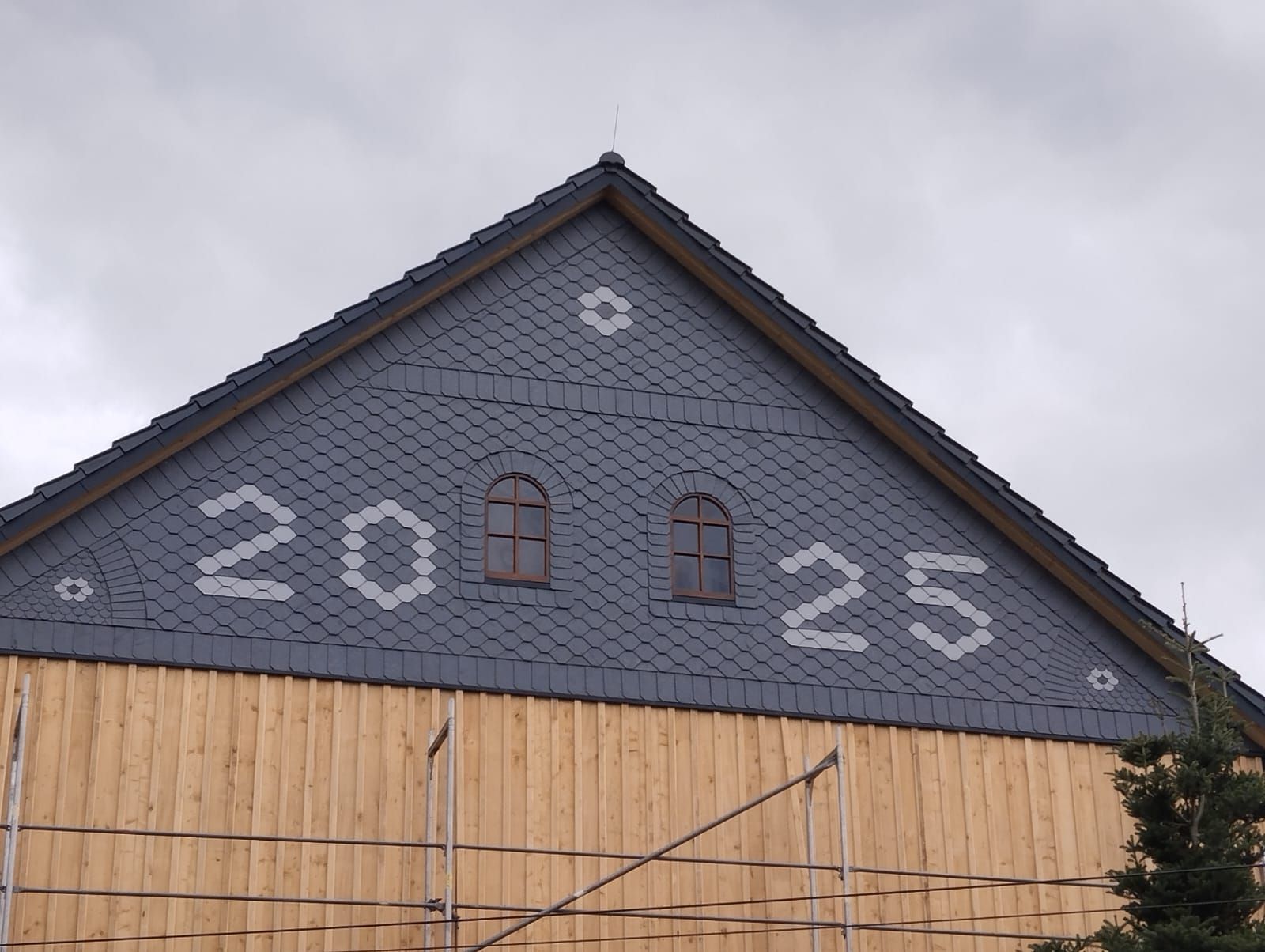 Schieferfassade mit dekorativer Jahreszahl 2025, kunstvolle Schieferdeckung an Giebelwand