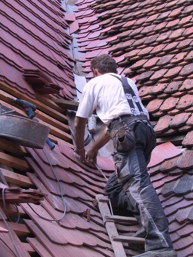 Dachdecker bei Reparatur eines Biberschwanzdachs, Verlegung von Dachziegeln an einer Kirche