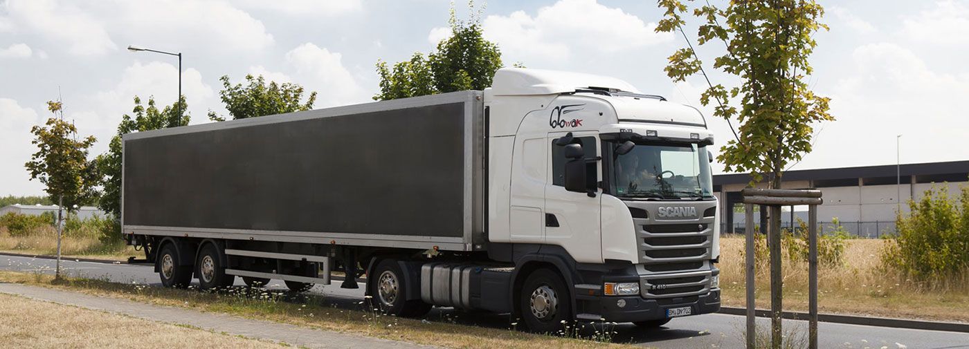 Ein weißer Lastwagen mit einem schwarzen Anhänger fährt eine Straße entlang