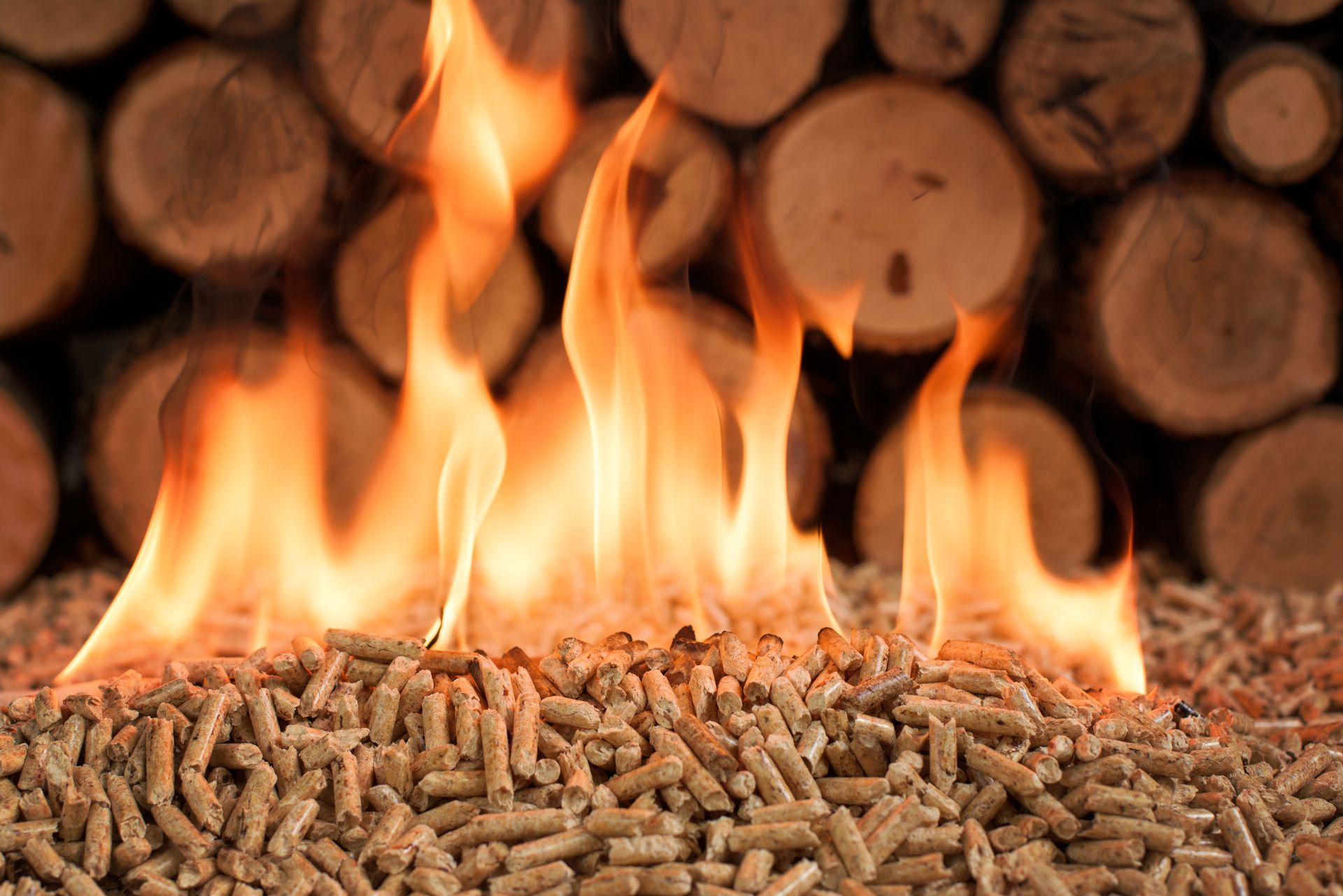 Des flammes sur des pellets avec des bûches en fond.