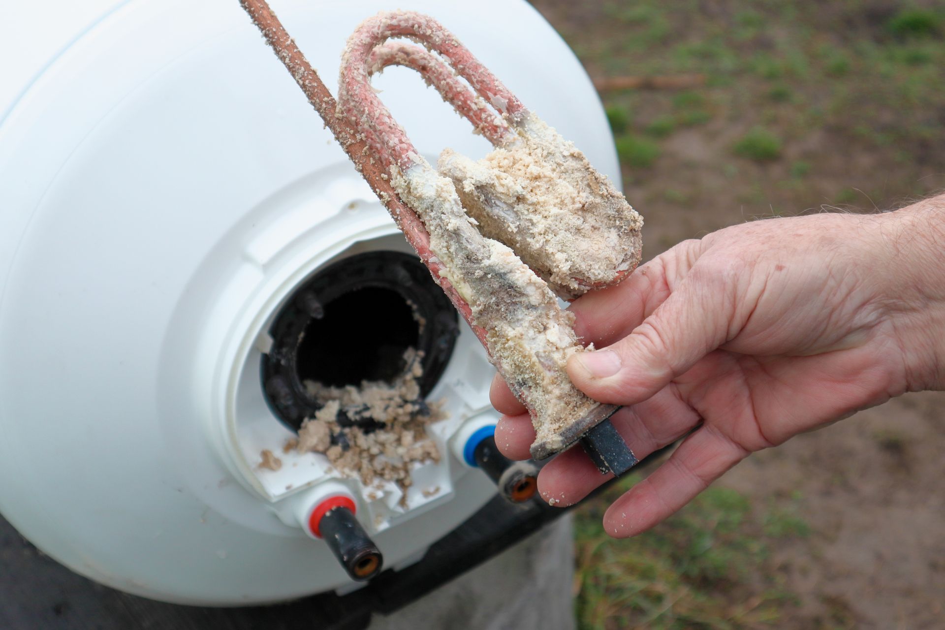 Une main tient la résistance d'un chauffe-eau recouverte de calcaire.