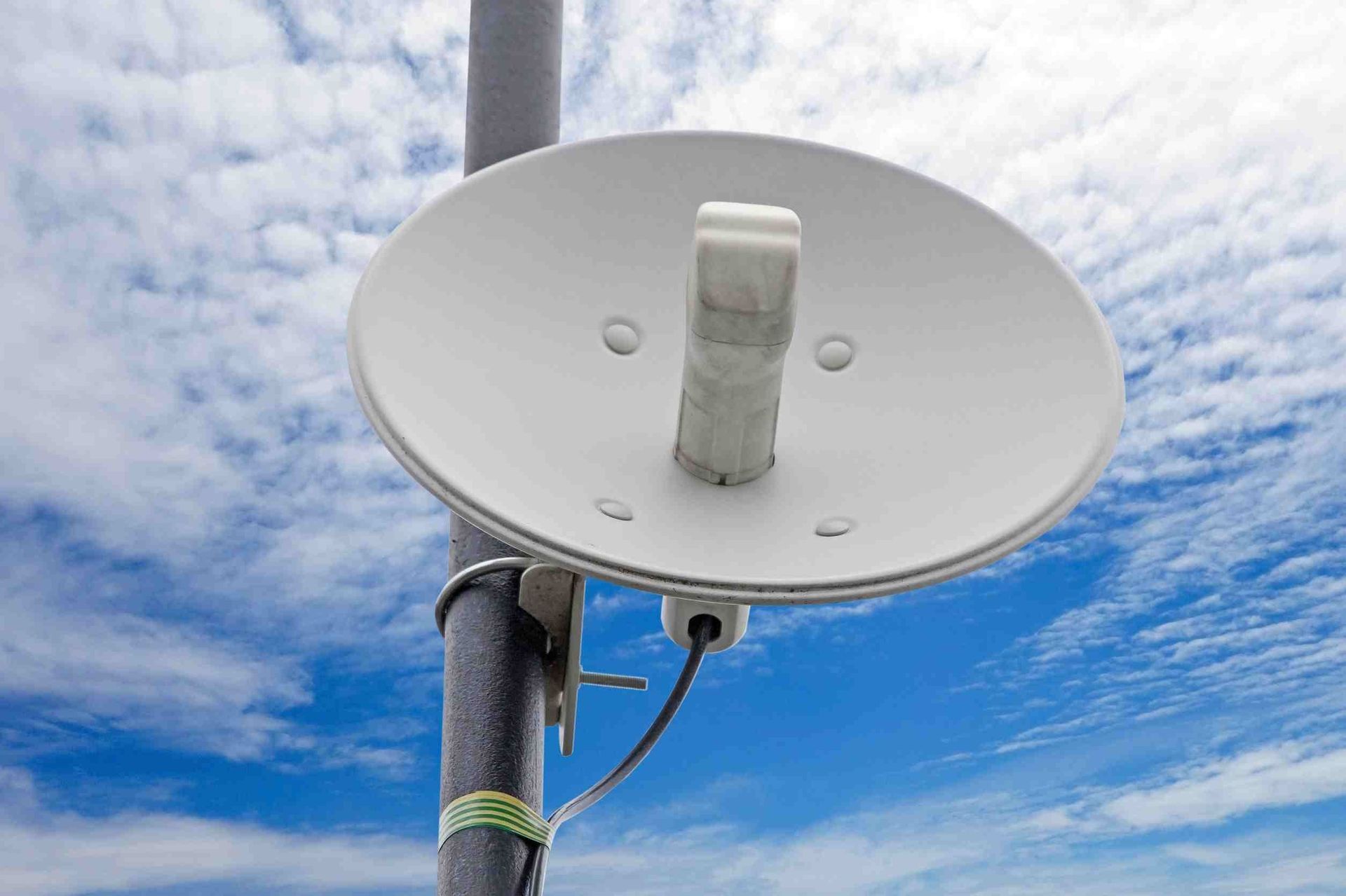 Una antena parabólica blanca está fijada a un poste con un cielo azul de fondo.