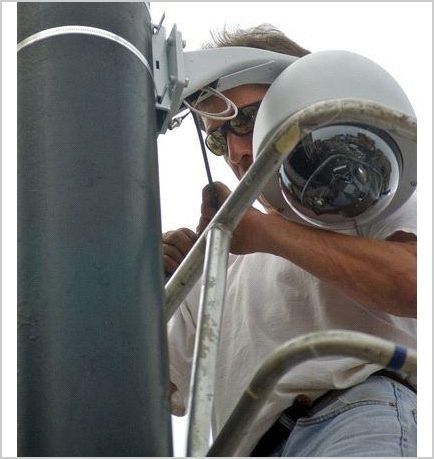 Un hombre está trabajando en una cámara en un poste.