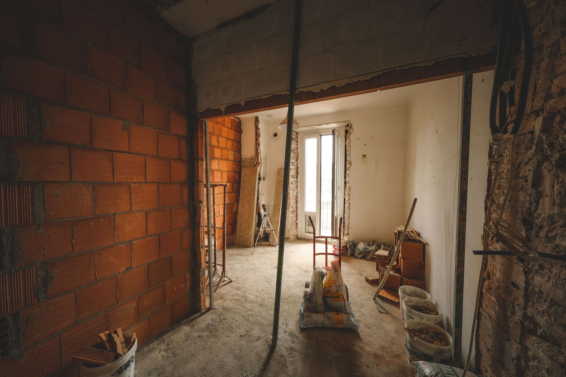 Habitación sin terminar en construcción, con paredes de ladrillo visto, escombros y cubos cerca de una puerta.