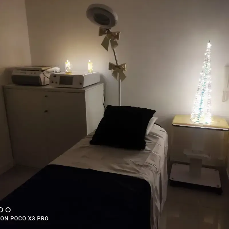 Una sala de spa con iluminación tenue, con una camilla de tratamiento, un dispositivo médico sobre un armario y un aro de luz