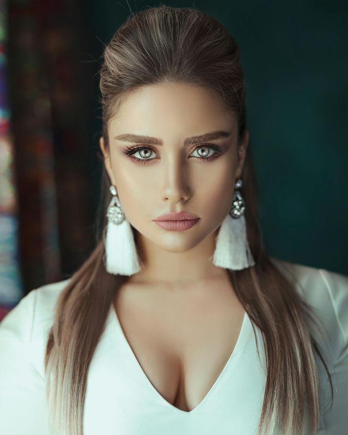 Una persona de ojos claros y cabello largo, que lleva grandes pendientes blancos con borlas y una blusa blanca