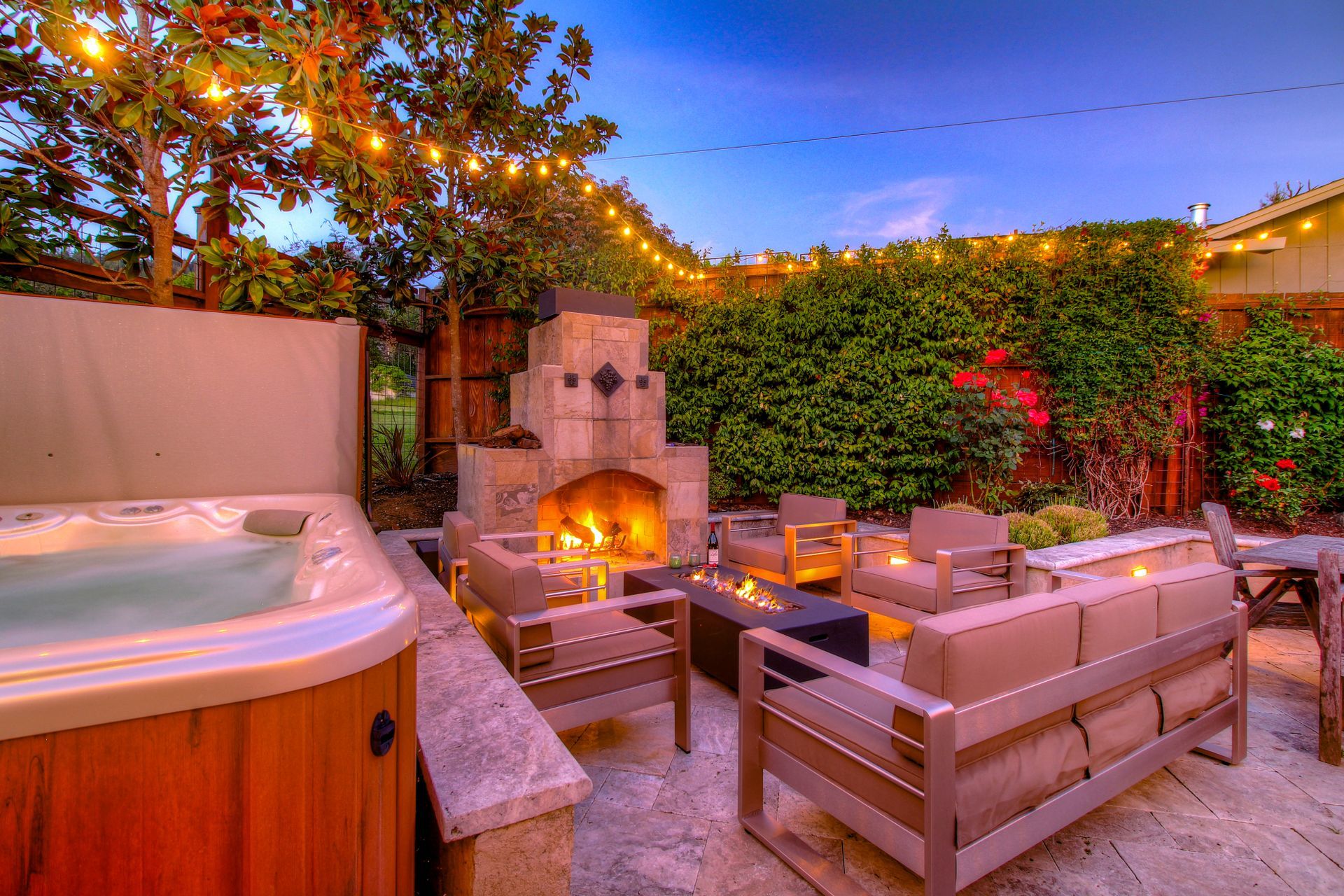 A patio with a fireplace , couch , chairs and a hot tub.