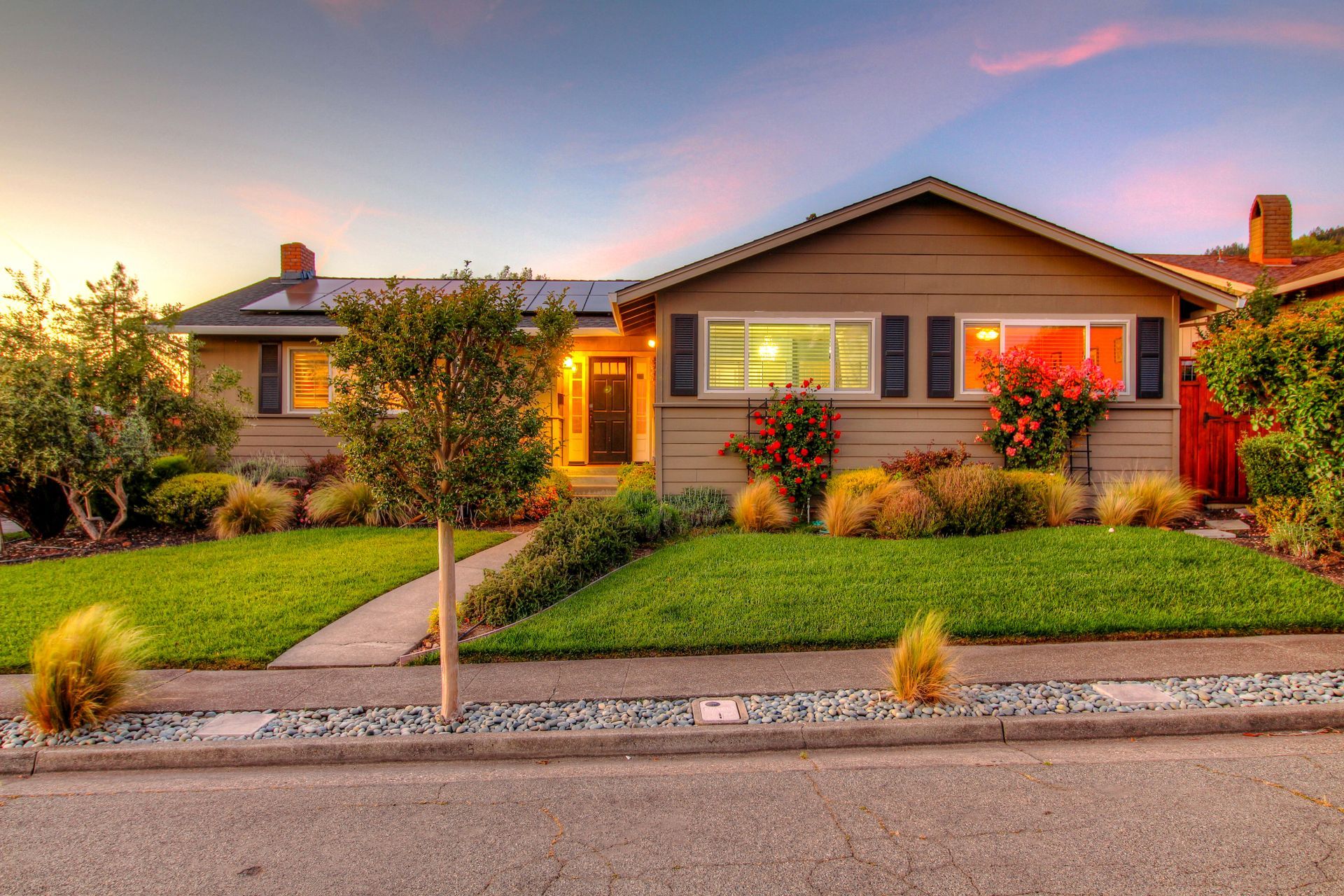 A house with a lush green lawn and a sunset in the background
