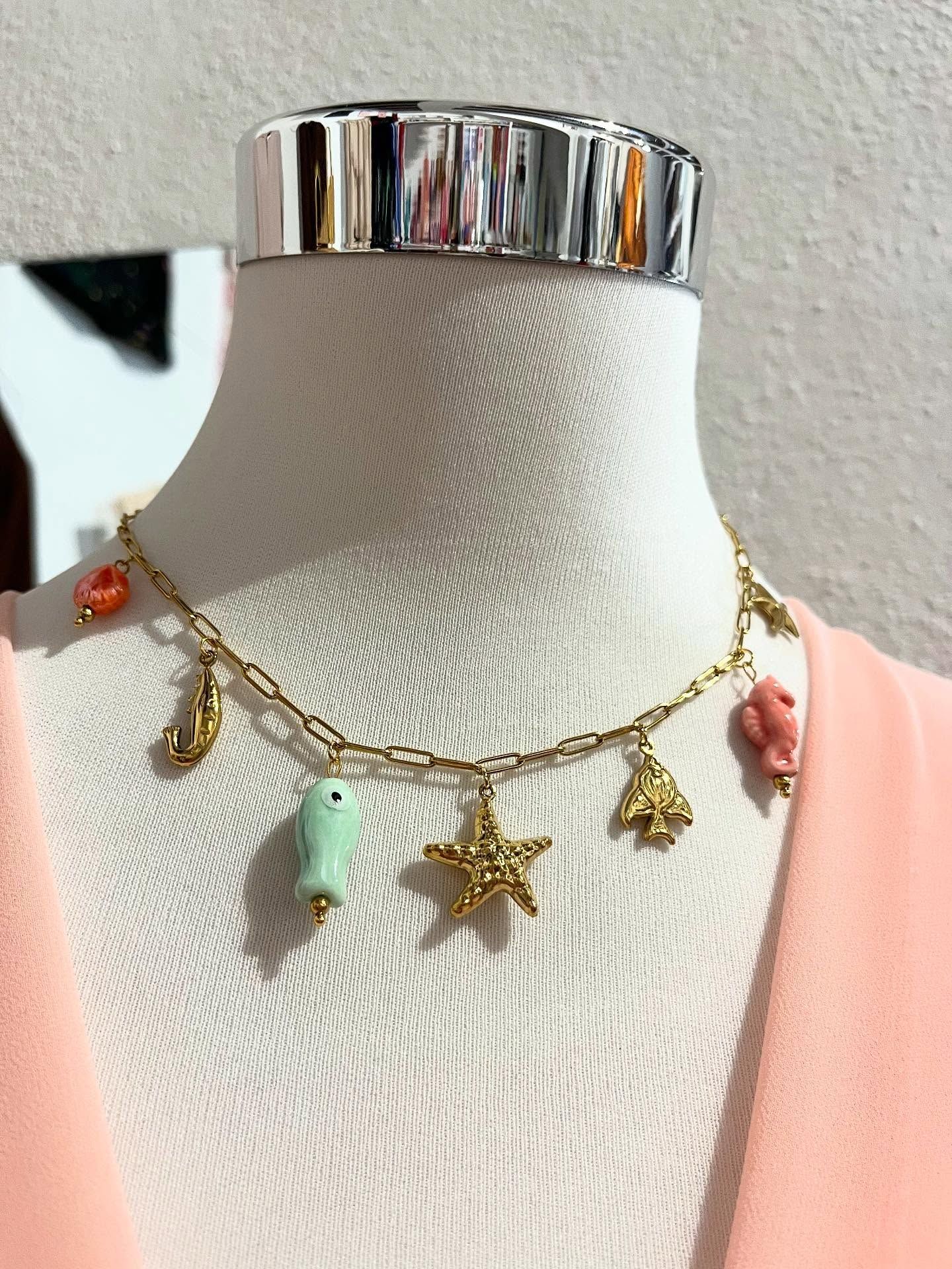 Collar de oro con dijes de conchas marinas sobre un maniquí blanco, sobre un fondo rosa.