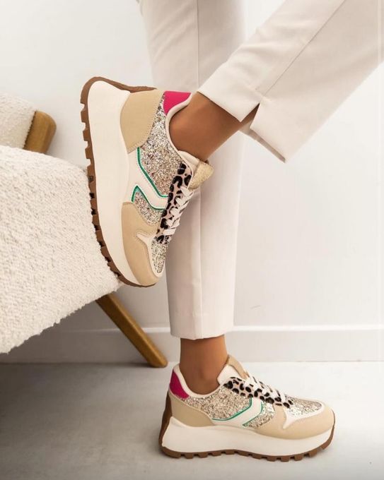 Persona que viste zapatillas de deporte de color beige, rosa y estampado de leopardo, apoyada en una silla blanca.