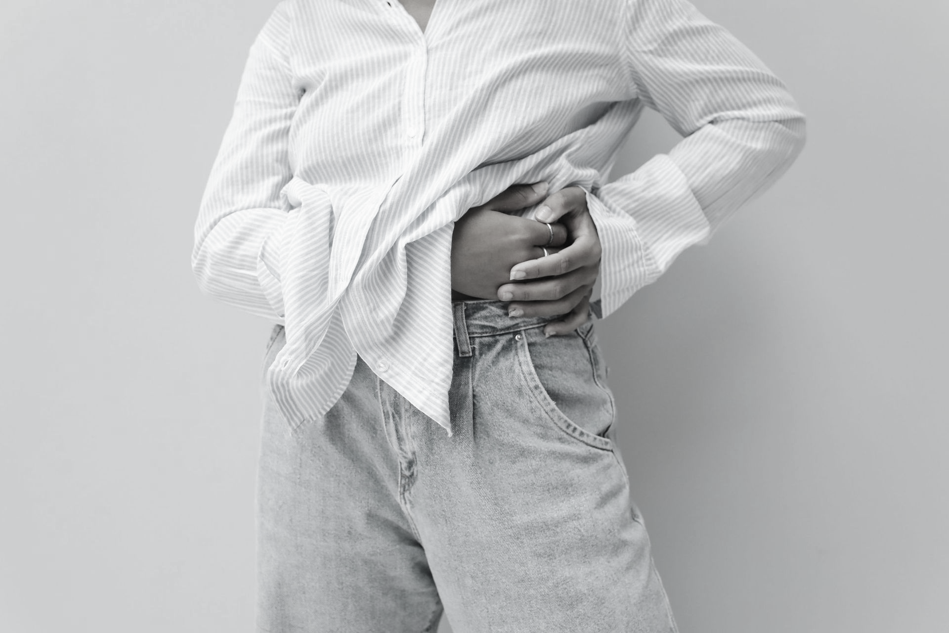 Person in hellblauem Hemd und Jeans hält sich den Bauch vor hellblauem Hintergrund