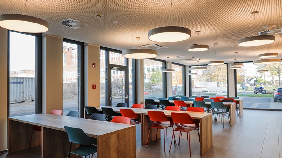 Ein großes Esszimmer mit Tischen und Stühlen und vielen Fenstern.
