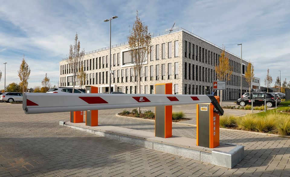 Ein Parkplatz mit Schranke vor einem großen Gebäude.