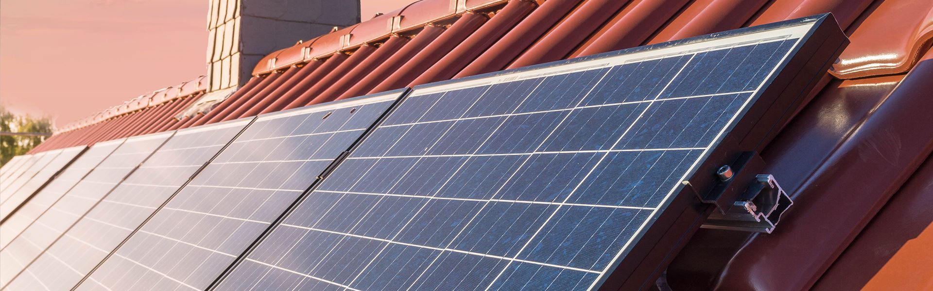 Eine Reihe von Solarmodulen auf einem Dach mit einem Schornstein im Hintergrund.