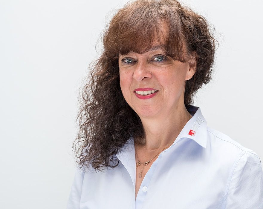 Eine Frau mit lockigem Haar trägt ein weißes Hemd und lächelt.