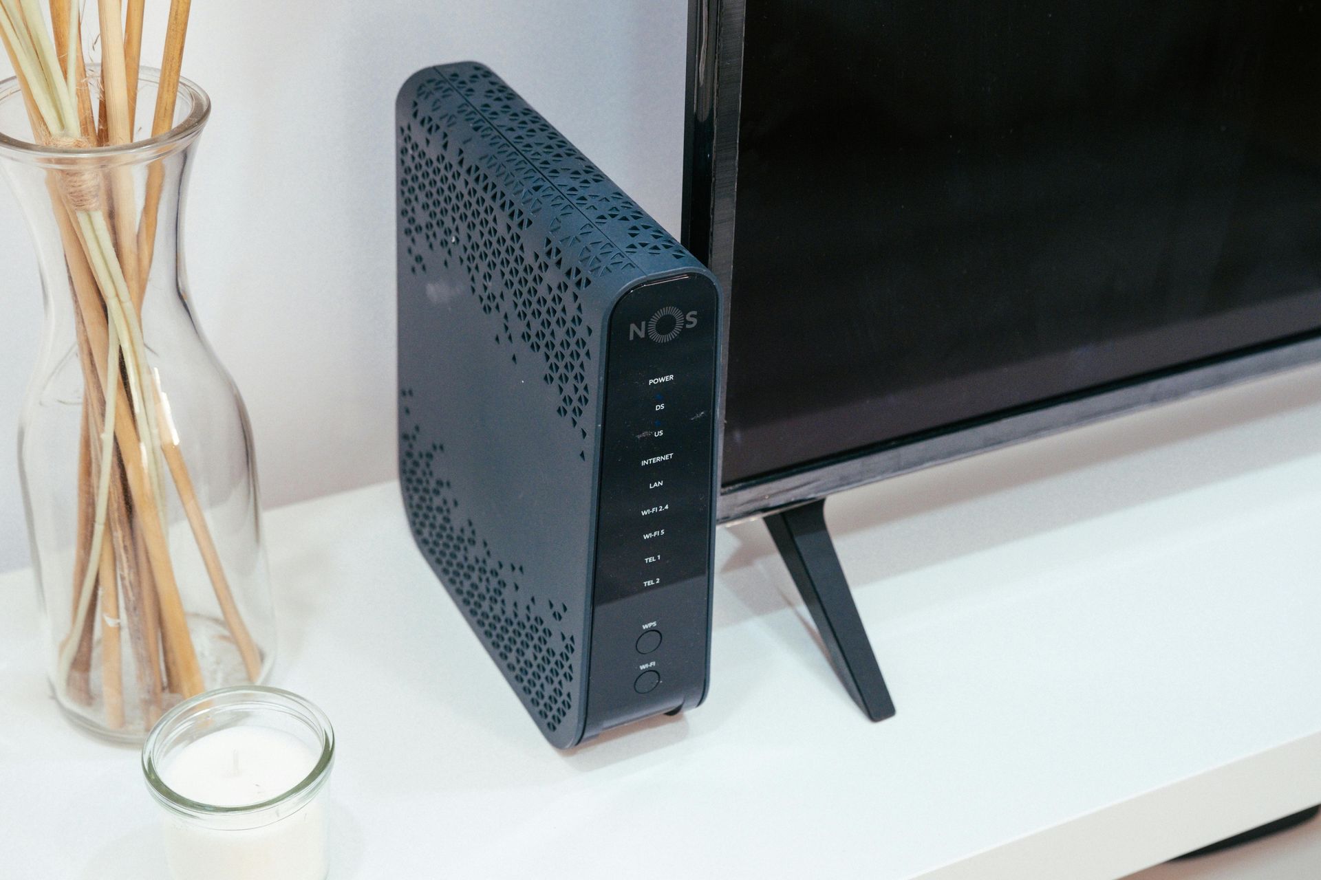 Ein Fernseher steht auf einem Regal neben einem Router und einer Vase mit Stöcken.