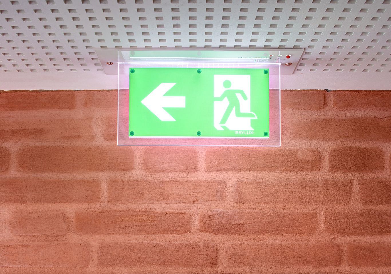 An einer Backsteinmauer hängt ein grünes Ausgangsschild.